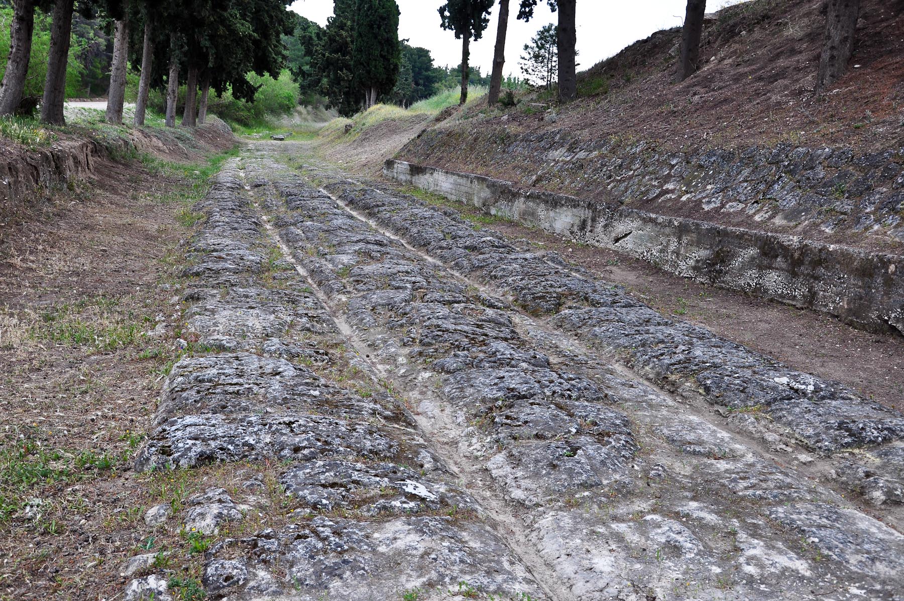 上图:哥林多铺石路(Corinth Diolkos)。哥林多城位于哥林多地峡(Isthmus of Corinth)西南方,这地峡连接希腊本土南部和伯罗奔尼撒半岛,西北有爱奥尼亚海(Ionian Sea)哥林多湾(Gulf of Corinth)的列该翁港(Lechaion),东南有爱琴海(Aegean Sea)撒罗尼克湾(Saronic Gulf)的坚革哩港(Cenchraea or Kechries)。在哥林多地峡运河开通之前,两湾之间的客旅与货物往来都经由这条铺石路中转。哥林多城以地利之便,坐收南北和东西方贸易路线上的各种税赋,所以被形容为「富裕之城」(wealthy city)。