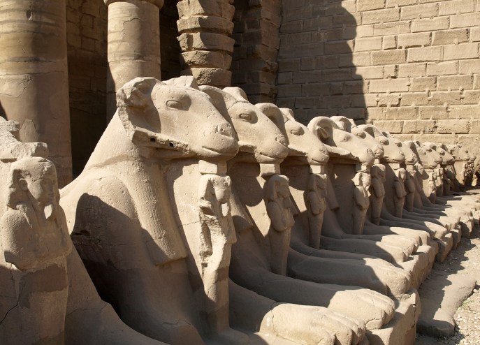 上图：建于主前2000年的古埃及卡纳克神庙（Temple of Karnak）入口的狮身公山羊像，公山羊象征古埃及最高神阿蒙-拉（Amun-Ra），站在公山羊脚前的是法老，象征最高神保护法老。多毛的公山羊是古实（Kush）的主神，埃及征服古实之后，认为古实主神就是太阳神阿蒙-拉，从此公山羊成为阿蒙-拉的化身之一。由于公山羊是多产的象征，所以公山羊形状的阿蒙神又与男性生殖神敏（Min）组合成阿蒙-敏（Amun-Min），进而演化成希腊淫乱的山羊神潘（Pan）。库努牡神（Khnum）也长着一个公羊头。